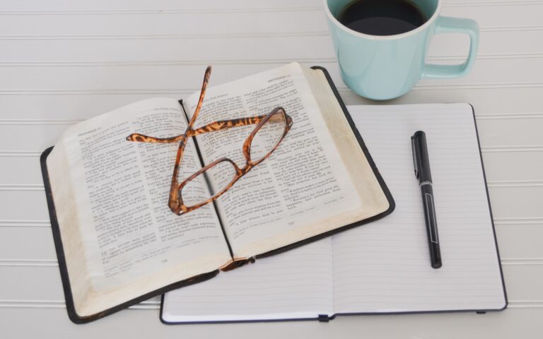 flat lay photography of tortoiseshell eyeglasses on top of bible near black pen and teal mug